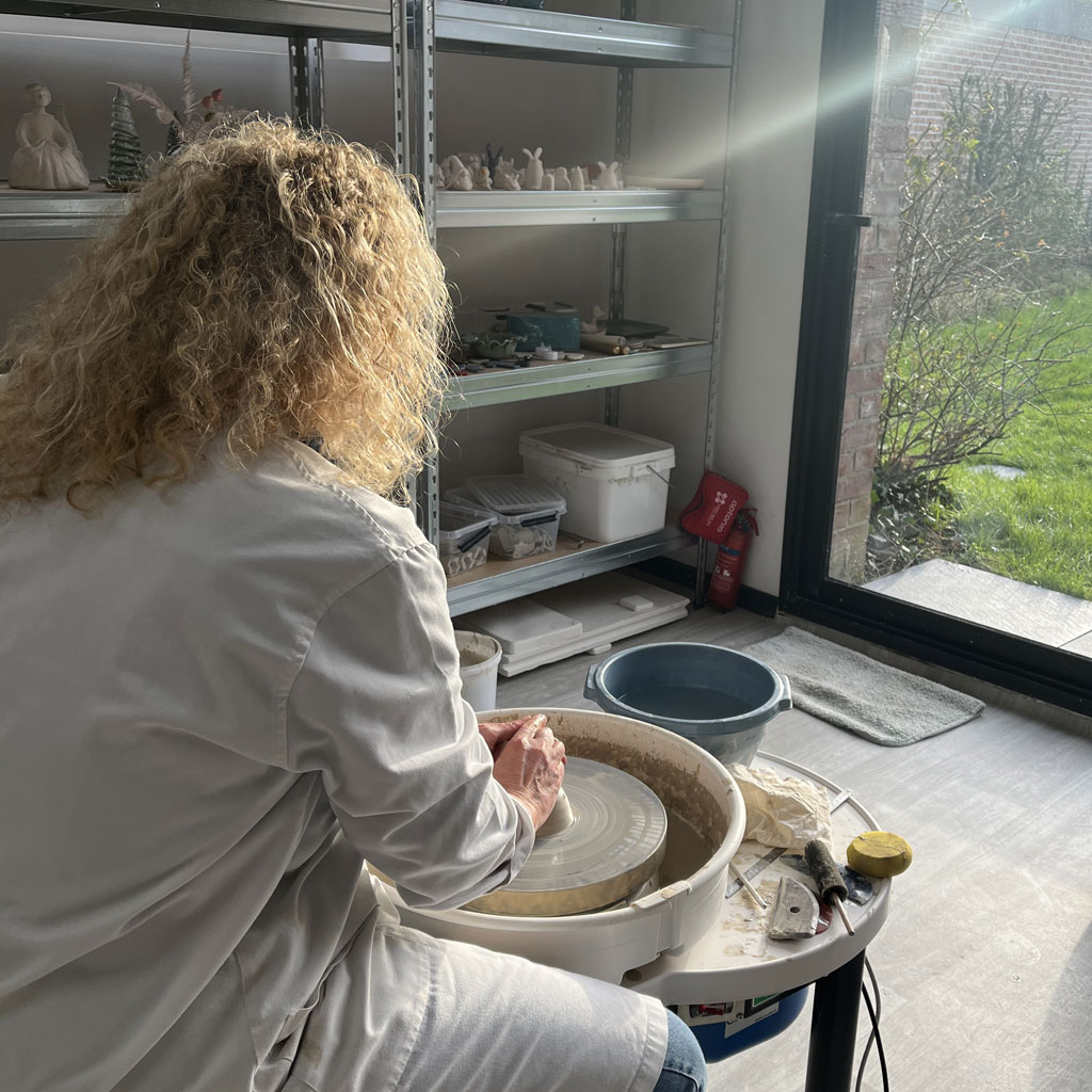 une femme dans un atelier de céramique en train de faire le tournage sur le tour de potier