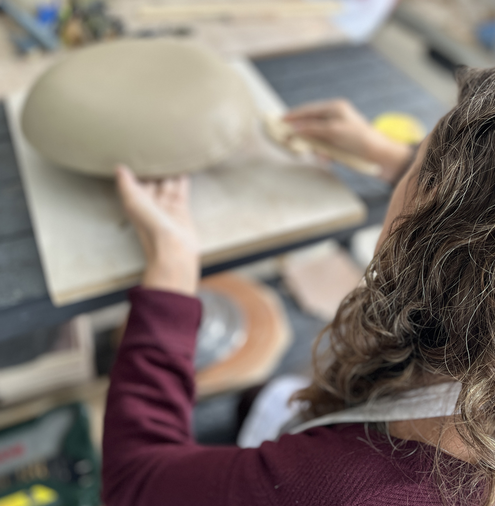 une jeune femme est en train de modeler un grand bol en argile à la plaque