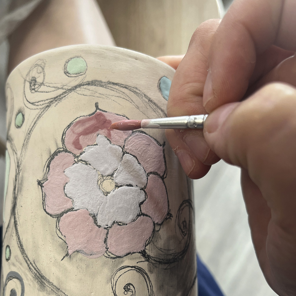 une main qui paint sur le vase céramique avec les couleurs à peindre