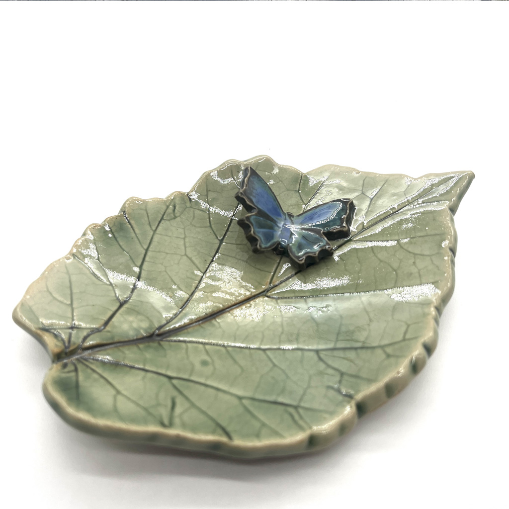 un porte savon en céramique en forme d'une feuille avec un papillon.